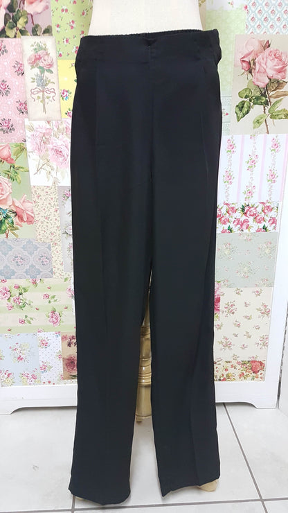 Black polyester long pants displayed against a floral background, with elastic at the back and a zipper with clip on the right side, featuring pleats detail on the front.